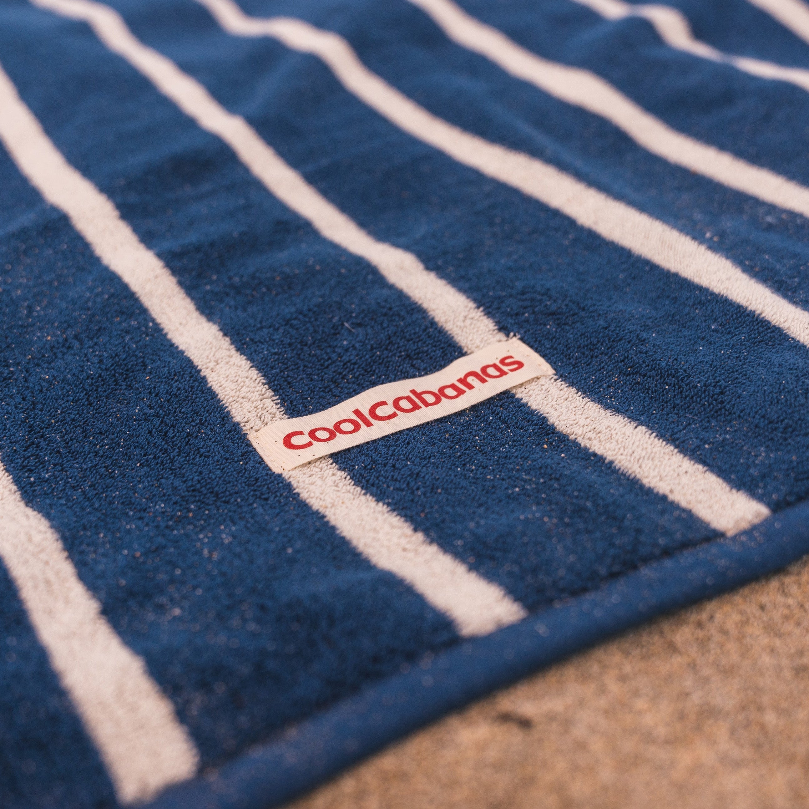 Blue towel with white stripes and 'cool cabanas' logo on a textured surface